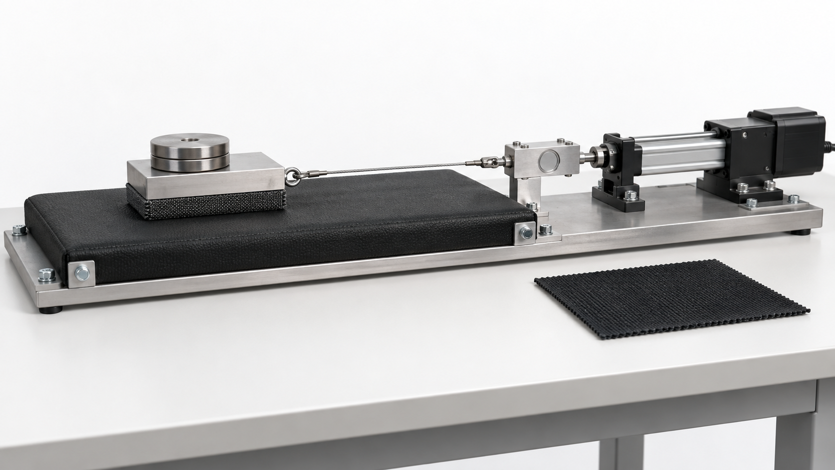 Proposed material-test apparatus: a weighted fabric-backed sled on a secured pad connected to a load cell and linear actuator.