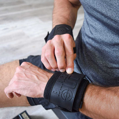 User securing Advanced Muscle Mechanics Black Out Premium Wrist Wraps, ensuring stability and protection for heavy lifts and strength training exercises.