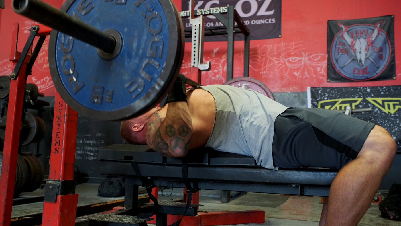Athlete in a gray top holding a loaded barbell near the bottom of a bench press while lying on The Launch Pad®.