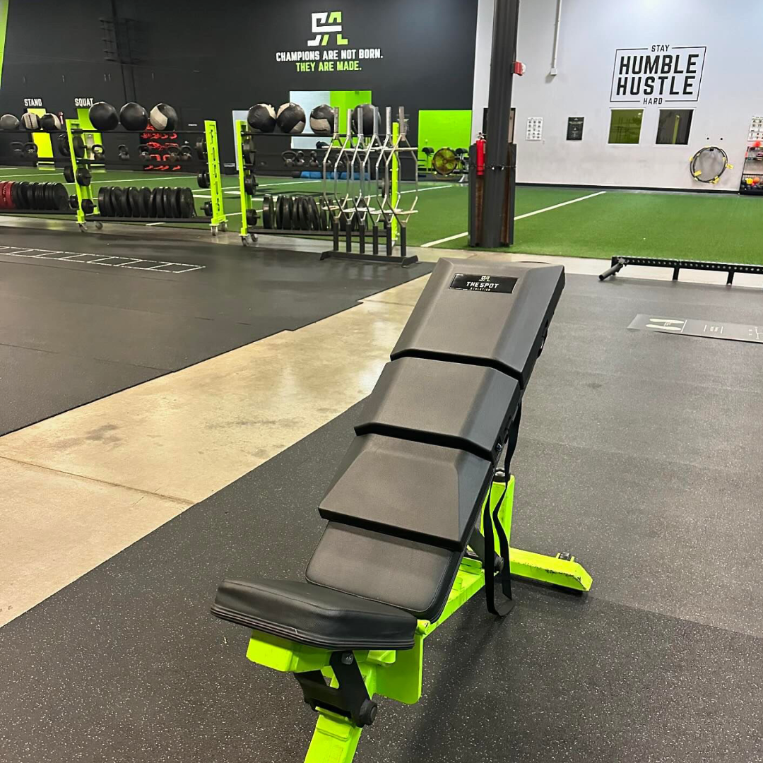 Adjustable bench equipped with The Spot Athletics custom Launch Pad™ in front of facility banners reading 'Champions Are Not Born' and 'Stay Humble Hustle Hard'
