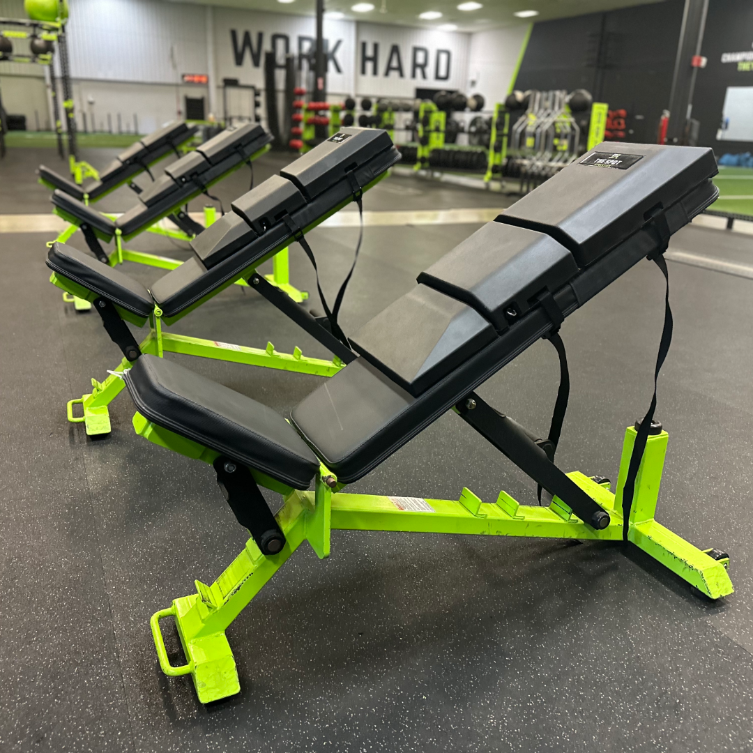 Four adjustable benches equipped with The Spot Athletics custom Launch Pads™ in front of the 'Work Hard' wall in a strength training facility.