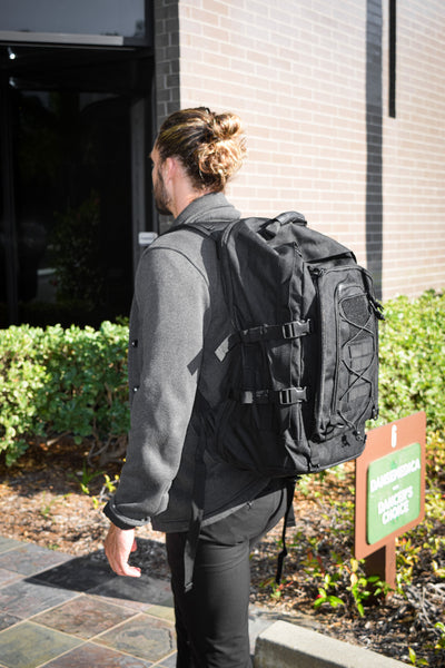 A man walks towards a building entrance while wearing the Advanced Muscle Mechanics tactical backpack, designed to carry the Launch Pad, highlighting its portability for on-the-go fitness training.