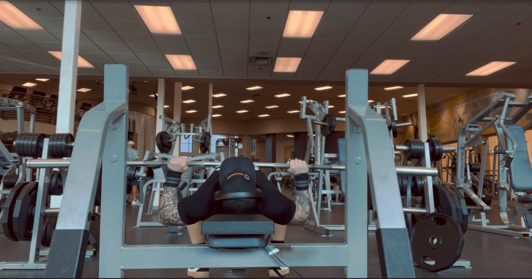 Front view of an athlete performing a barbell bench press while lying on The Launch Pad® in a gym.